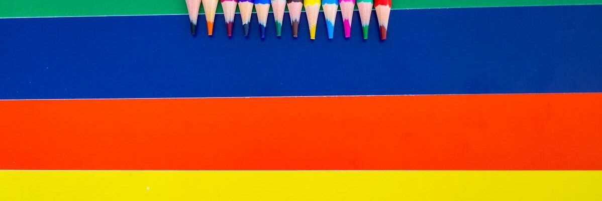 A collection of colored pencils arranged on a bright striped background, showcasing vivid rainbow hues.